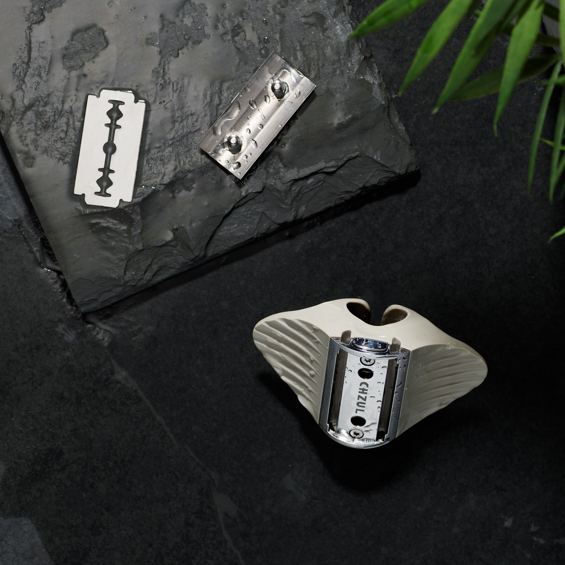 Razor and razor blades on a dark stone surface with a plant in the corner.
