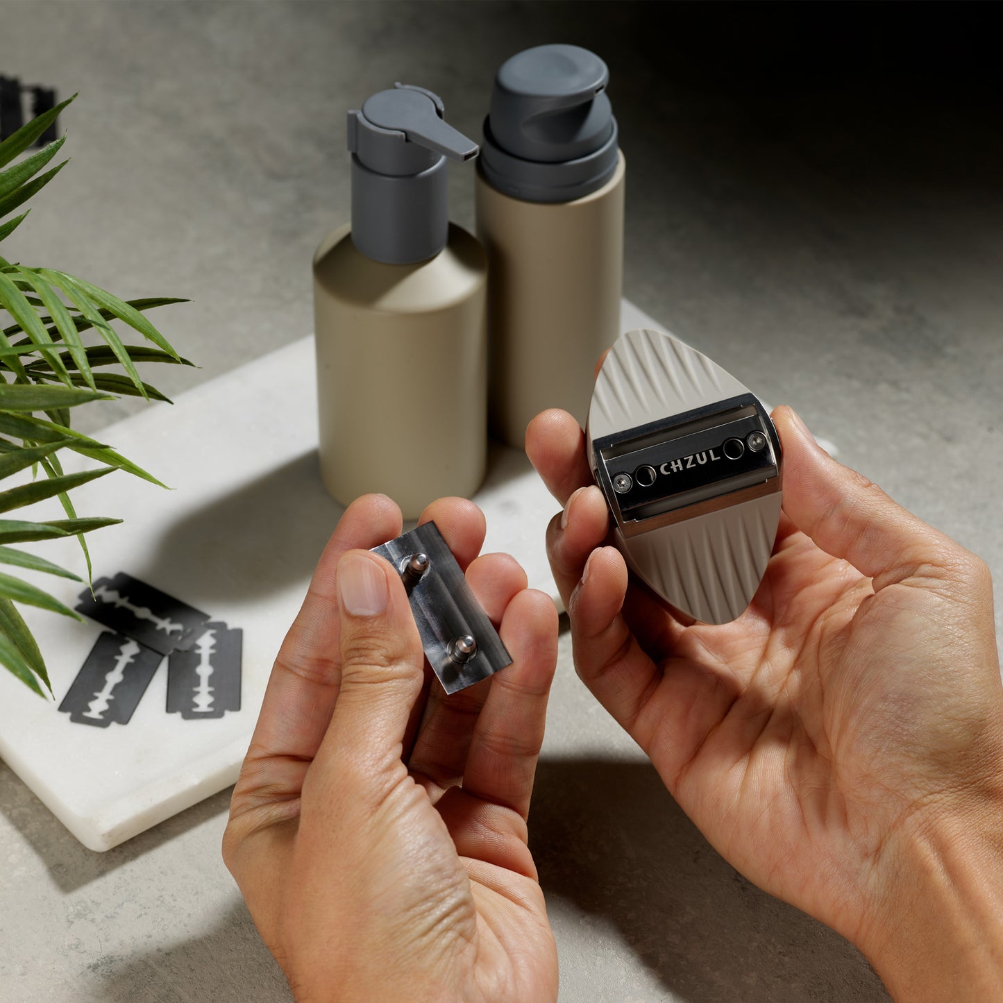 Person holding a razor and razor heads with a blurred background of bottles and a plant.